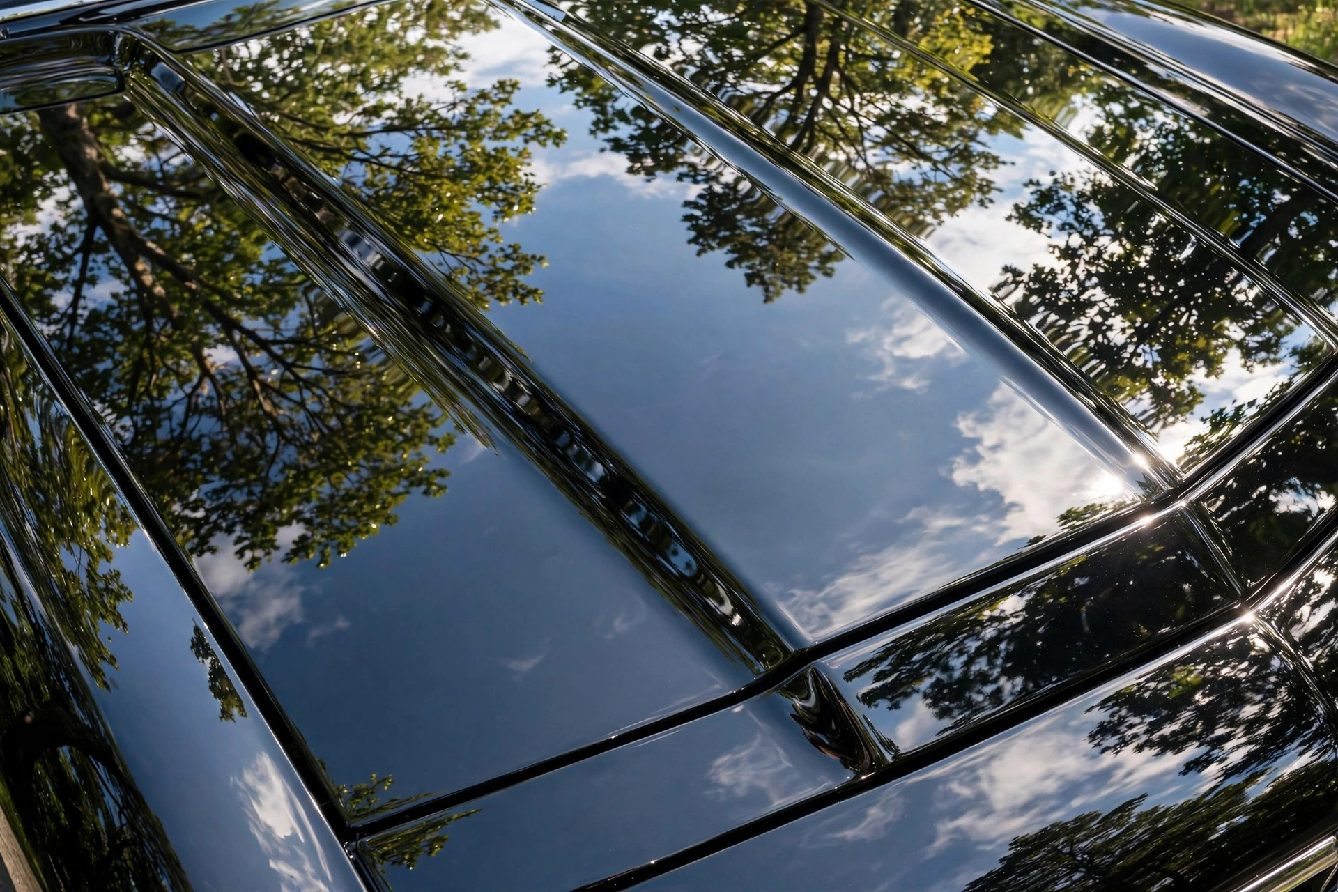 Deep black car hood with mirror reflections in flawless clear coat